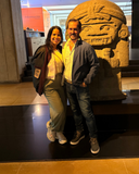 Two people posing in front of a large stone sculpture in an indoor setting.